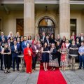 A group of UQ researchers holding award trophies standing out the front of a sandstone building on a red carpet